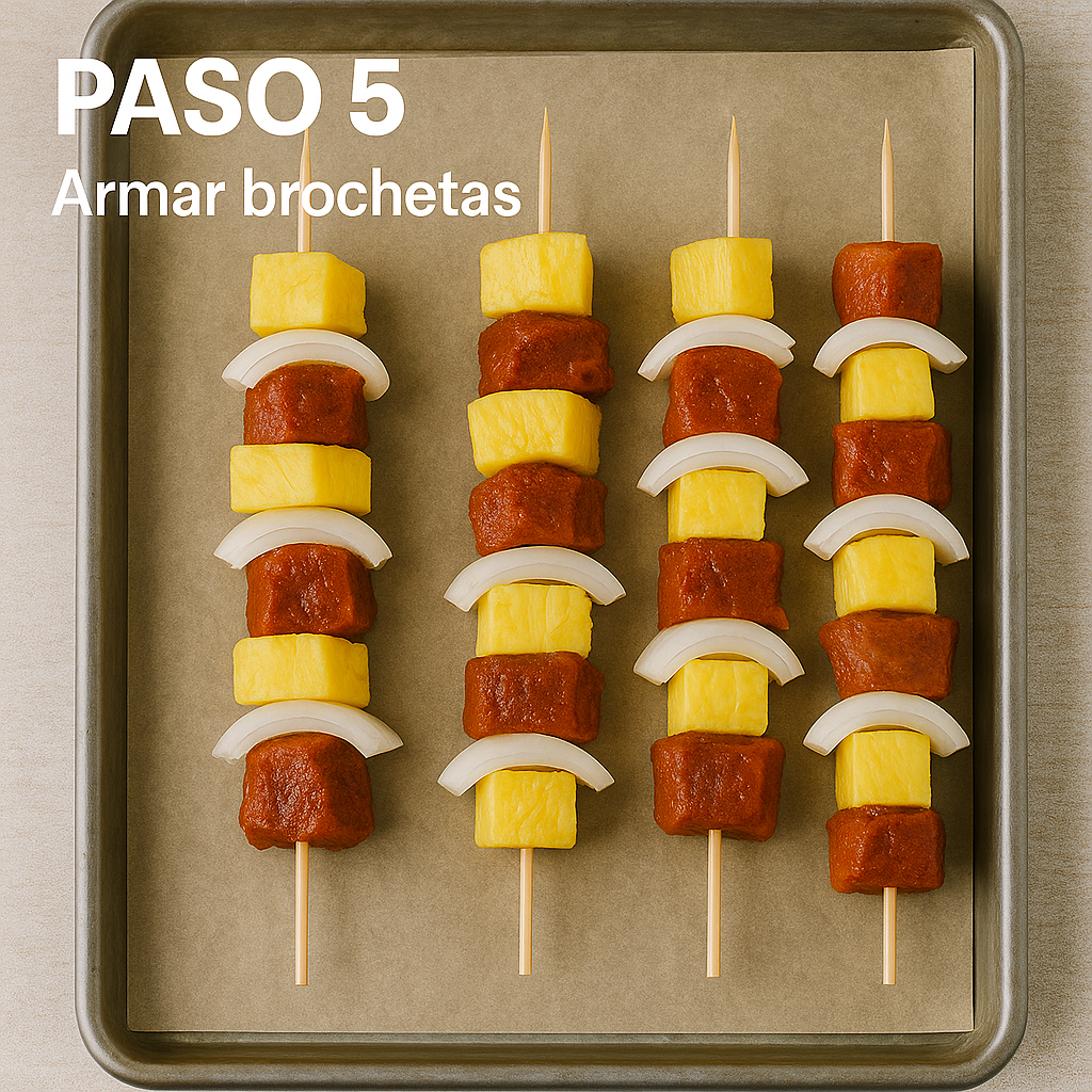 Brochetas con carne al pastor, piña y cebolla sobre bandeja con papel de horno listas para cocinar.